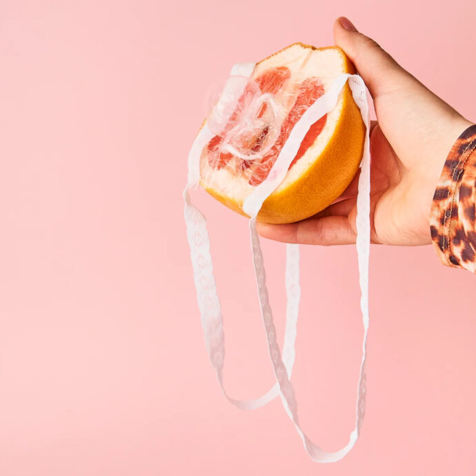 Female hand holding up half of a grapefruit with a female condom covering it